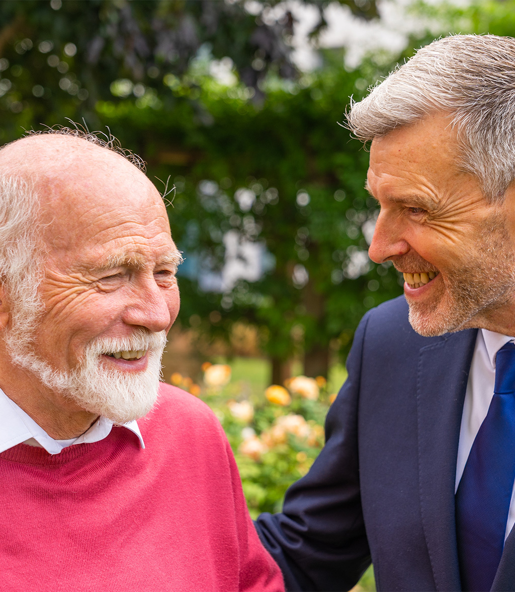 Elderly Resident and Care Home Manager share a laugh in a green garden